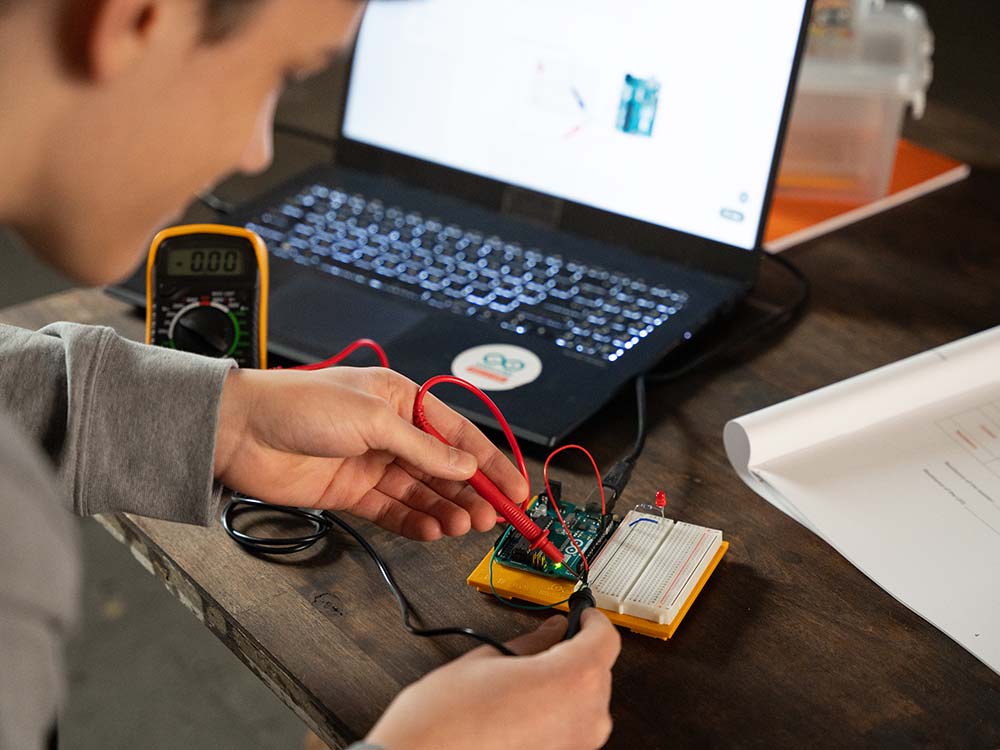 Person working on a electronic project with a laptop and multimeter